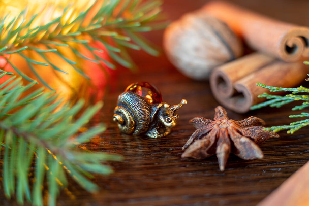 Σύνθεση Χριστουγέννων ή Πρωτοχρονιάς με ενθύμιο φιγούρας σαλιγκαριού δίπλα σε έλατο, ξυλάκια κανέλας και κάρδαμο. Επιλεκτική εστίαση - Φωτογραφία, εικόνα