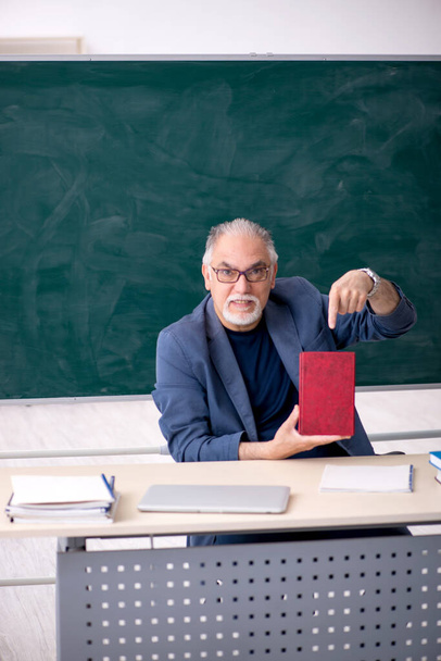 Vieux professeur masculin tenant livre dans la salle de classe - Photo, image