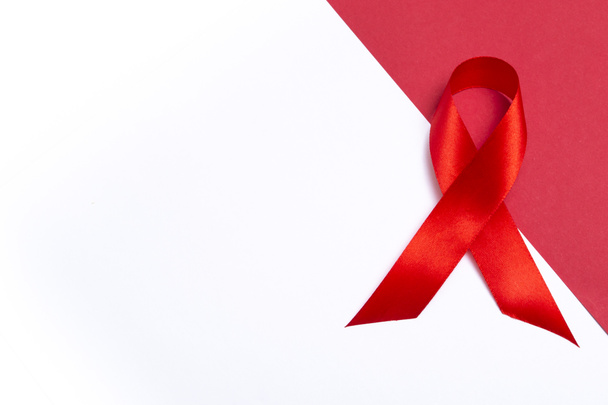 Concepto médico para el Día Mundial del SIDA en diciembre. Cinta roja de sensibilización sobre el sida sobre fondo blanco y rojo. Cerrar espacio de copia - Foto, imagen