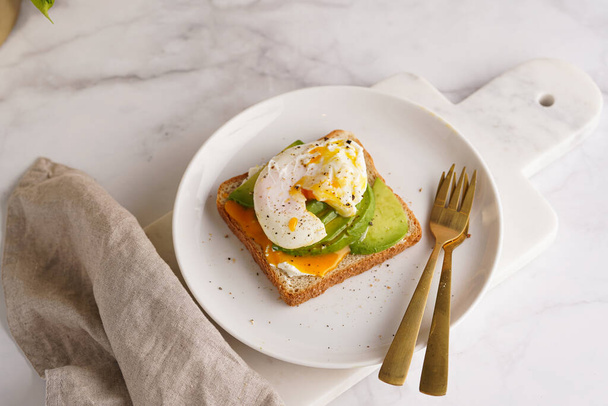 Savoury breakfast - A toast bread with cream cheese, avocado and poached egg on a white plate on marble tray - 写真・画像