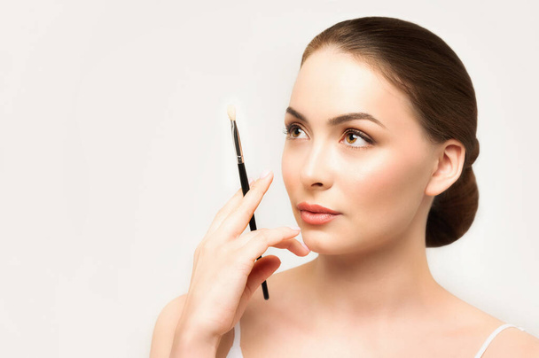 Model doing makeup. Caucasian girl thinks about make-up with brush in her hand - Φωτογραφία, εικόνα