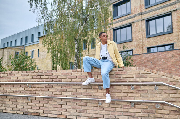 Young male photographer sitting on the brick wall - Zdjęcie, obraz