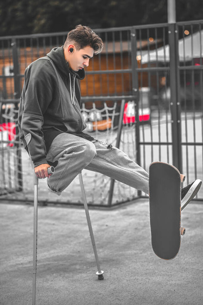 Guy appuyé sur des béquilles et touchant skateboard avec pied - Photo, image