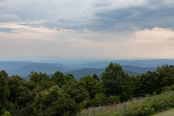 Kuzey Carolina 'nın Blue Ridge Dağları' nın derin bulutlu manzarası, puslu atmosfer, yuvarlanan çimenler ve ağaçların ön planı, yatay görünüm - Fotoğraf, Görsel