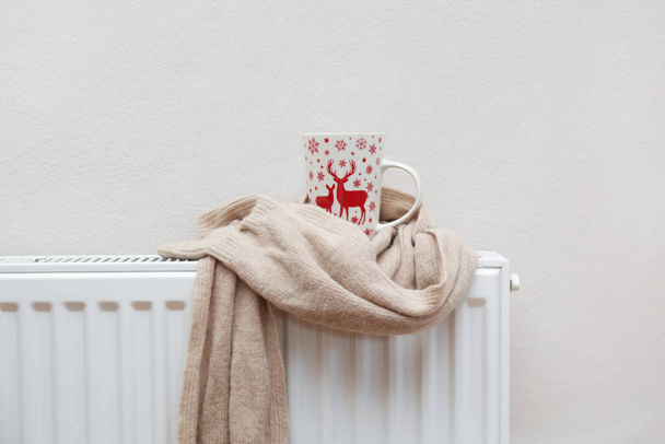 Фото чаю, загорнутого у вовняний шарф на радіаторі. концепція опалювального сезону
.  - Фото, зображення