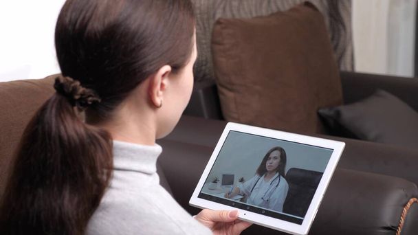 Médico profesional trata a un paciente en un chat de vídeo en línea. Una joven cayó enferma en casa usando una tableta digital para hablar con su médico. Aplicación de videoconferencia médica. Médico de familia - Foto, Imagen