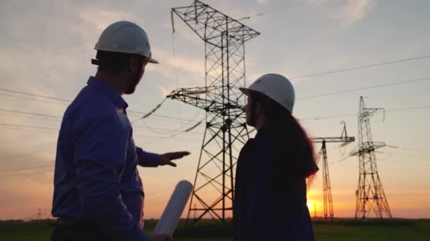 Two construction engineers work together on an electrical transmission line. Teamwork of power engineers in protective helmets, maintenance of power lines in the open air. Colleagues shake hands. - Footage, Video