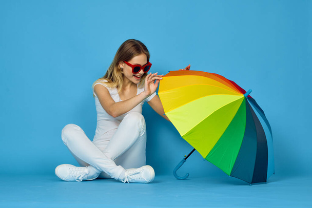 fashionable woman with umbrella rainbow colors posing blue background - Foto, imagen