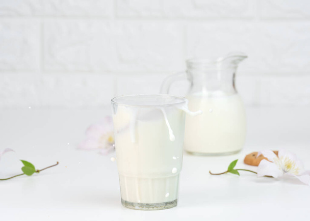 plný skleněný šálek čerstvého mléka se stříkancemi stojany na bílém stole, zdravá snídaně - Fotografie, Obrázek