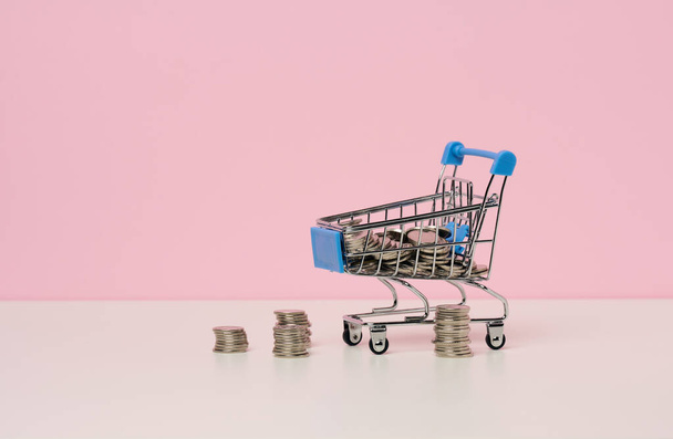 ミニチュア金属ショッピングカートと白いテーブルの上のコインの山。割引や販売、予算の節約の概念。オンライン取引 - 写真・画像