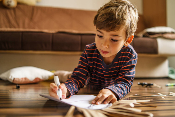 Small caucasian boy playing on the floor at home using crayon to draw on the paper toy homemade art developing new skill - leisure activity playful kid growing up concept - Foto, Bild