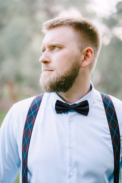 Bearded man in blue shirt with suspenders and bow tie, close-up  - Foto, afbeelding
