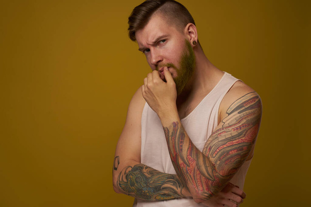 γενειοφόρος άντρας με λευκό μπλουζάκι με τατουάζ στα χέρια του, με σοβαρή εμφάνιση. - Φωτογραφία, εικόνα