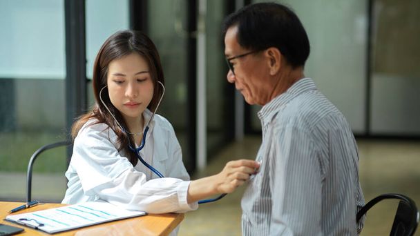 A young female doctor uses a stethoscope to check the pulse of an aged male patient. heart rate, heart beat. - Photo, Image