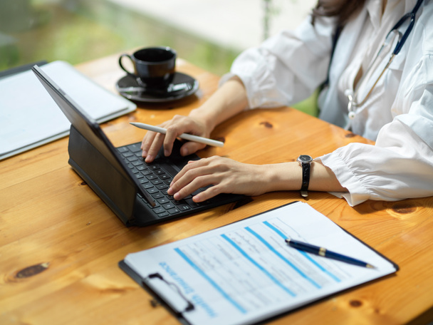 Обрізане зображення жінки-лікаря, що працює на цифровому планшетному комп'ютері, кавовій чашці та медичному звіті на столі
. - Фото, зображення