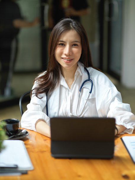 Портрет веселой азиатской женщины-врача сидит за рабочим столом в офисе, работая на планшетном сенсорном экране. - Фото, изображение