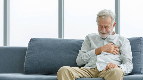 biały stary starszy seniorzy niezdrowe chore mężczyzna mąż dziadek siedzi na kanapie w domu sam trzymając się za ręce na klatce piersiowej mając awaryjny kardio problem cierpi z powodu pilnego zawału serca choroba. - Zdjęcie, obraz