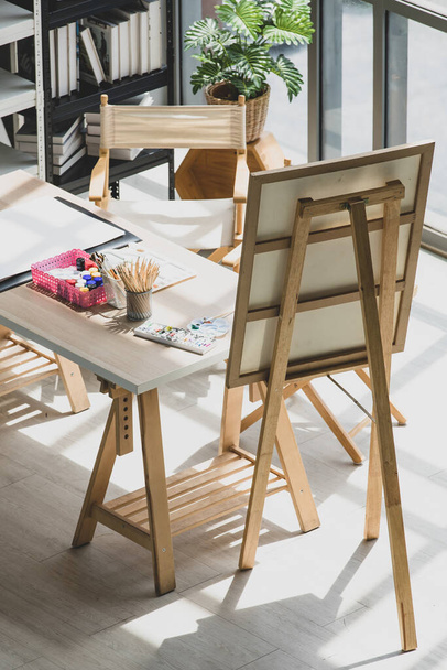 Vista superior de dibujo pintura artista hobby taller estudio equipo en mesa de madera incluyendo lienzo caballete pie acuarela pincel lápices paleta bandeja papel bajo fuerte luz desde el exterior. - Foto, Imagen