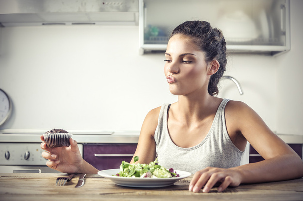 Young girl deciding whether to eat a healty salad or a muffin - Photo, image