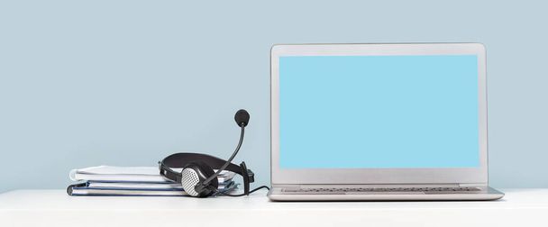 Side view of slim laptop with headphones headset on white desk. Mockup screen. Distant learning. working from home, online courses or support. Audio podcast. Helpdesk or call center banner - Photo, image