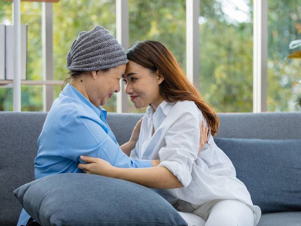 Oudere Aziatische vrouw patiënt bedekt het hoofd met kleding effect van chemo behandeling in kanker genezing proces aanraken van haar dochter voorhoofd met gelukkig. - Foto, afbeelding
