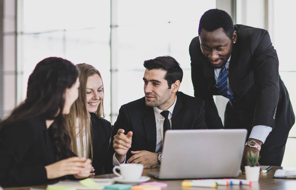 Líder profissional de negócios africano adulto apontando e consultando estratégia de planejamento com colegas caucasianos concentrados que se reuniram na frente do laptop enquanto estavam sentados na mesa de trabalho do escritório - Foto, Imagem