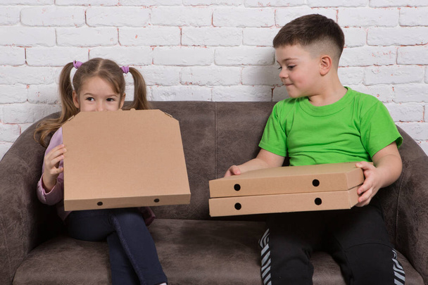 chlapec a dívka na pohovce, držící krabice od pizzy, usmívající se a nakukující do krabice, koncept - Fotografie, Obrázek