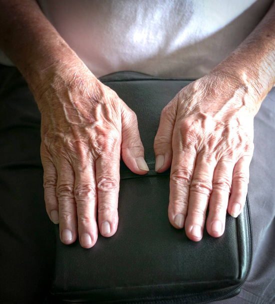 Wrinkled hands of senior man on top of a book. Selected focus on his thumbs. - Photo, image