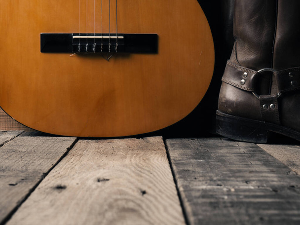 Old cowboy boots with an acoustic guitar on barn wood, space for your text - Photo, image