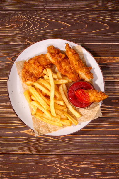Assiette avec de savoureuses frites, ailes de poulet frites et sauce tomate sur table en bois - Photo, image