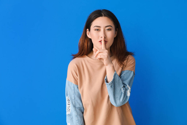 Junge Asiatin zeigt Schweigegeste auf farbigem Hintergrund - Foto, Bild