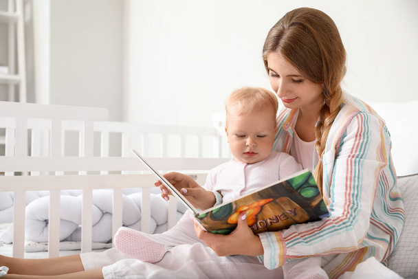 Genç anne, küçük tatlı bebeğine kitap okuyor. - Fotoğraf, Görsel
