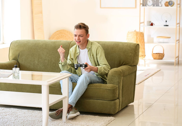 Ευτυχισμένο έφηβο αγόρι που παίζει βιντεοπαιχνίδι στον καναπέ στο σπίτι - Φωτογραφία, εικόνα