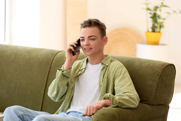 Teini-ikäinen poika puhuu matkapuhelimella sohvalla kotona - Valokuva, kuva