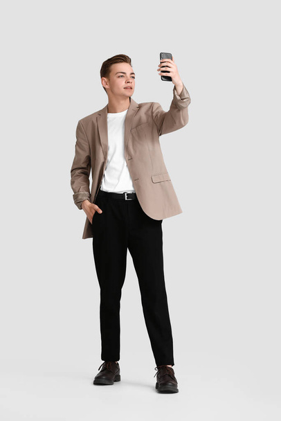 Teenage boy with mobile phone taking selfie on white background - Foto, afbeelding