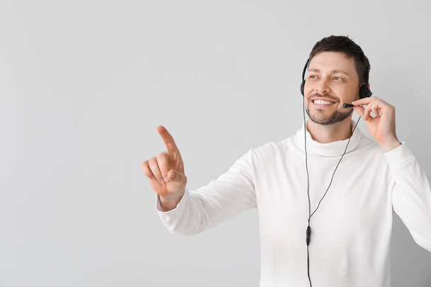 Smiling consultant of call center in headset pointing at something on light background - 写真・画像