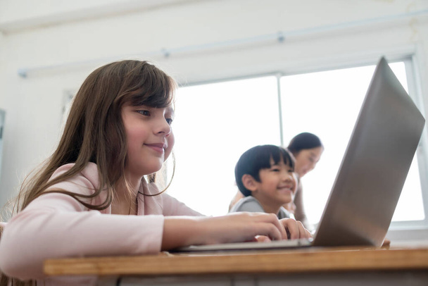 Happy Hymyilevä pieni söpö tyttö käyttää kannettavaa tietokonetta opiskellessaan luokkahuoneessa kansainvälisessä koulussa. Koulutus ja verkko-oppiminen teknologian avulla - Valokuva, kuva