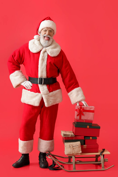 Happy Santa Claus with letters and gifts on sledge against color background - Photo, Image
