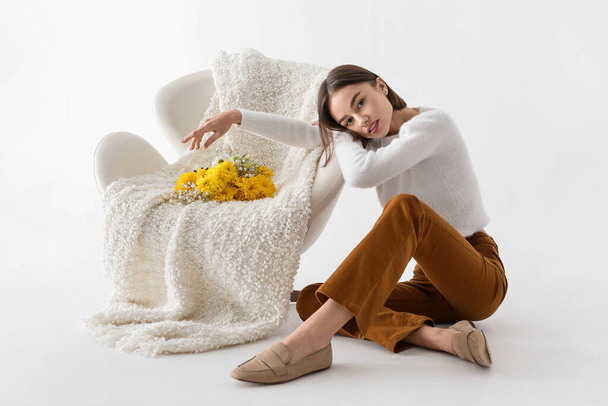 Beautiful young woman near armchair with bouquet of flowers on white background - Photo, Image