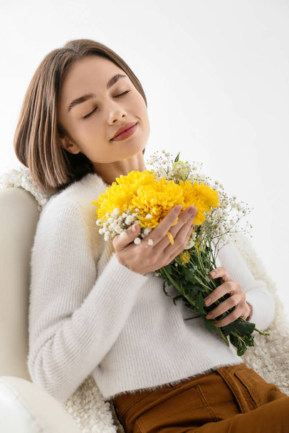 白い背景にアームチェアに座って花の花束を持つ美しい若い女性 - 写真・画像