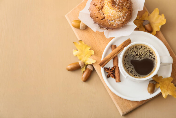 Cup of coffee with acorns, autumn leaves and cupcake on color wooden background - Photo, image