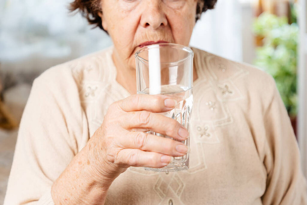 Senior woman holds a glass of water. Taking medications for pain. Close up. The concept of caring for the elderly. - Foto, afbeelding