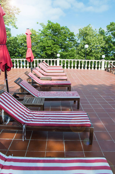 Leere Holzliegestühle mit rot-weiß gestreiften Matratzen stehen in einer Reihe. Luxus-Outdoor-Erholung, vertikale Foto. - Foto, Bild