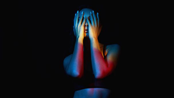 Sexy woman in Underwear. Beautiful Girl in Rainbow color lights. Model covering her face with hands  - Фото, изображение