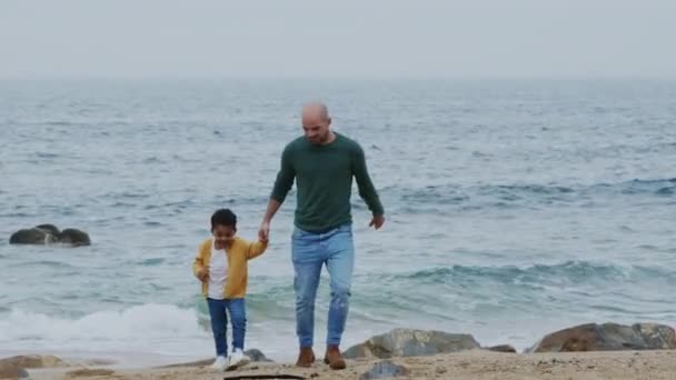 Отец гуляет с маленьким сыном на берегу океана - Кадры, видео