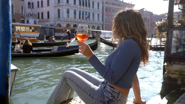 Ragazza tiene in mano e beve un bicchiere di Spritz, nella città dell'amore - aperitivo, bevanda alcolica Spritz Camapari o Aperol - bevanda tipica veneziana a base di vino bianco, arancia - Ponte di Rialto  - Foto, immagini