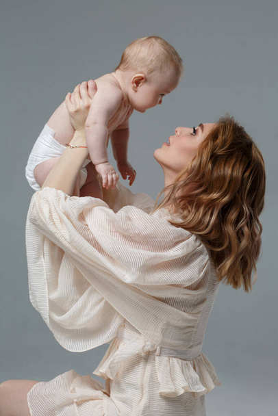 Mãe segura um bebê bonito em seus braços isolados em um fundo cinza. - Foto, Imagem