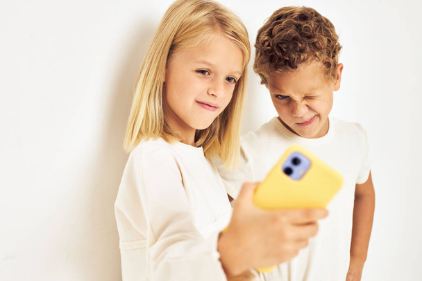 Молода весела дитина дивиться на телефон, що позує світлий фон
 - Фото, зображення