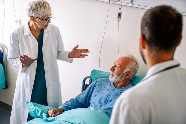Doctor talking to senior male patient in hospital bed who is recovering from the disease. Healthcare, coronavirus, people concept. - Foto, Imagen