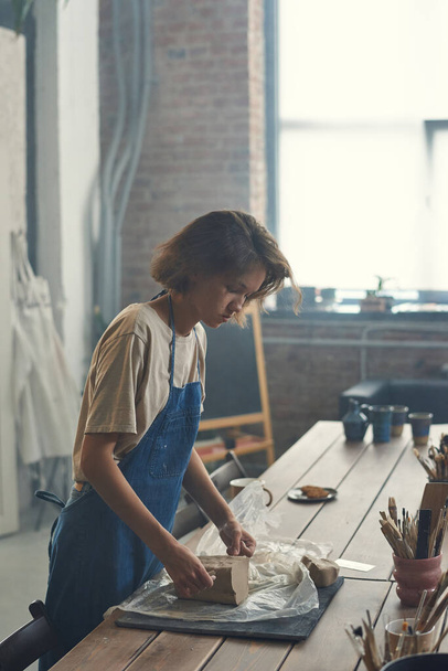 Молодая женщина-мастер керамики работает с глиной за столом - Фото, изображение